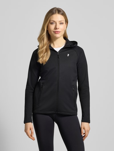 Modelka kobieca nosi Softshell-Jacke mit Kapuze Modell 'RIDER' von PEAK PERFORMANCE, czarna, krój regular fit, materiał z domieszką stretchu, z kapturem i zamkiem, detal z logo, widok całej sylwetki z przodu.