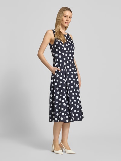 Frauenmodel trägt Cocktailkleid im Allover-Look von Vera Mont in Dunkelblau mit weißen Punkten, A-Linie, Material-Mix mit Stretch-Anteil, Midikleid, Rundhalsausschnitt, Rückenlänge bei Größe 36: 32 cm, Brustweite bei Größe 36: 36 cm, Ganzkörperansicht von vorne.