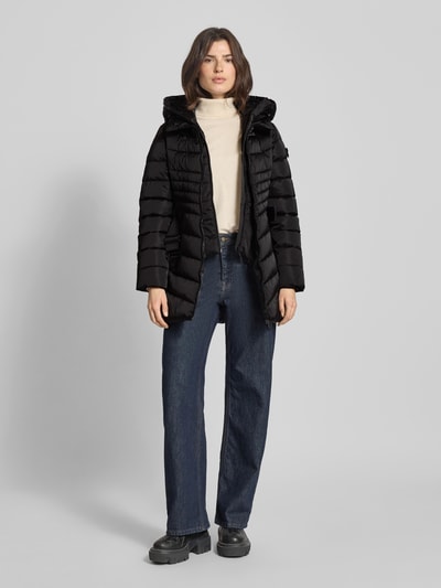 Frauenmodel trägt schwarzen Regular Fit Steppmantel mit Kapuze Modell 'KINA' von khujo, PU-beschichtet, Reißverschluss, Ganzkörperansicht von vorne.