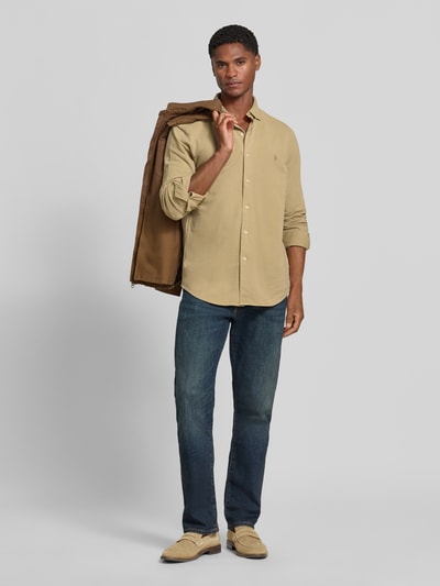 Männermodel trägt Slim Fit Freizeithemd aus reiner Baumwolle von Polo Ralph Lauren in Beige mit blauer Jeans und braunem Sakko, Ganzkörperansicht von vorne.