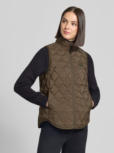 Kobiece modelka nosi kamizelkę o kroju regular fit z efektem pikowania Model 'Evy' od Didriksons, kolor brązowy, detal z logo, zamek błyskawiczny, długość tyłu w rozmiarze 36: 63 cm, szerokość ramion w rozmiarze 36: 37 cm, szerokość w rozmiarze 36: 46 cm, widok całej sylwetki z przodu.