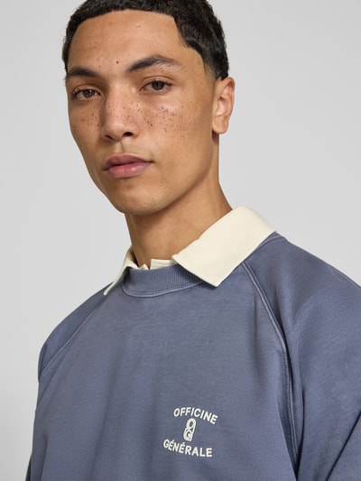 Männermodel trägt Sweatshirt aus reiner Baumwolle von Officine Générale in Blau mit Rundhalsausschnitt und Raglanärmel, Nahaufnahme Oberkörper.