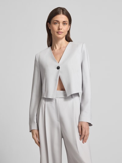 Frauenmodel trägt Asymmetrisch geschnittener cropped Blazer-curated by Vicky Heiler von SIC aus Viskose-Elasthan-Mix in Hellgrau, mit V-Ausschnitt, Knopfverschluss, Ganzkörperansicht von vorne.