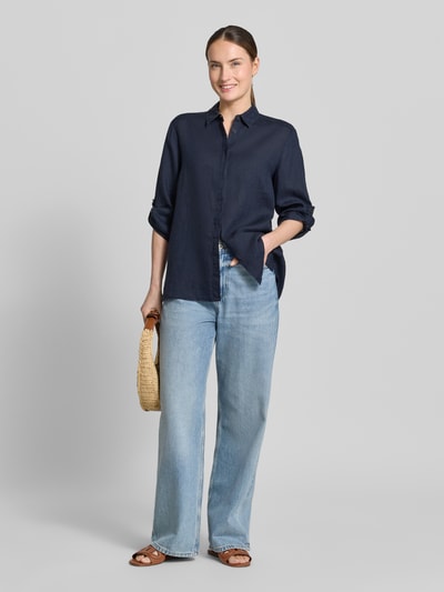 Vrouwenmodel draagt Relaxed Fit linnen blouse met 3/4-mouw model Clay van TONI, zuiver linnen, overhemdkraag, verborgen knoopsluiting, ruglengte maat 36: 63 cm, mouwlengte maat 36: 36 cm, donkerblauw, lichte jeans, stro tas, sandalen, ganzebodyaanzicht van voren.