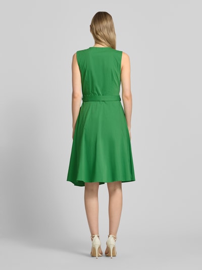 Vrouwenmodel draagt 'Kleid mit V-Ausschnitt in Wickel-Optik' van More & More in groen, katoenmix, getailleerd, mouwloos design, afneembare tailleband, ruglengte maat 36 100 cm, borstwijdte 36 35 cm, getextureerde stof, geheel zicht van achteren.