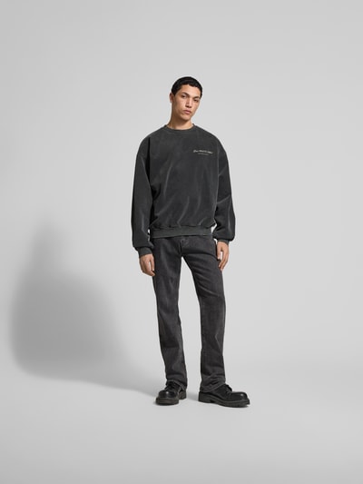 Männermodel trägt Oversized Sweatshirt aus Baumwoll-Mix von Don't Waste Culture in Dunkelgrau mit Statement-Print, Ganzkörperansicht von vorne.