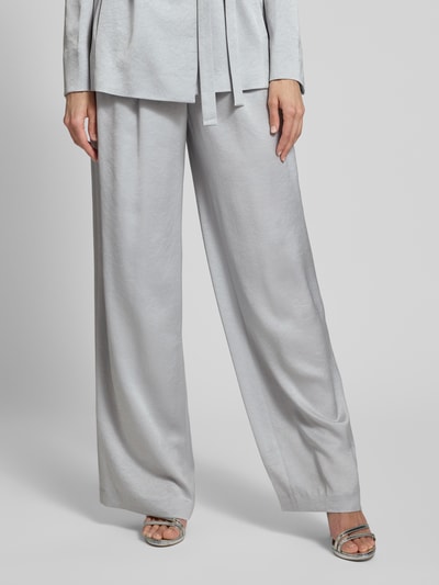 Kobiece model prezentuje Wide Fit Stoffhose mit gelegten Falten od Marc Cain, mieszanka acetatu, wpuszczane kieszenie, zapięcie na haftkę i zamek błyskawiczny, jasnoszary kolor, długość wewnętrzna nogawki 83 cm, szerokość w rozmiarze 36: 38 cm, spodnie materiałowe, widok z przodu na całe nogi