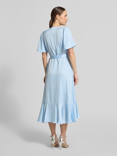 Frauenmodel trägt Cocktailkleid mit Volantsaum Modell 'THEA' von YAS aus blauem Satin, taillierter Schnitt, Midikleid, Schmetterlingsärmel, Ganzkörperansicht Rückansicht.