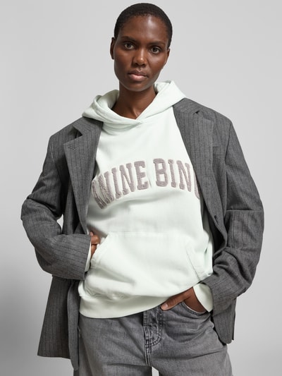 Frauenmodel trägt Oversized Hoodie mit Logo-Stitching von Anine Bing in Reine Baumwolle, Oversized-Fit, Kapuze, Känguru-Tasche, Rückenlänge 64 cm, Ganzkörperansicht von vorne.