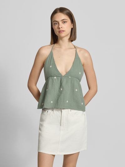 Frauenmodel trägt Crop Top aus reiner Baumwolle Modell 'THYRA RIO' von Only in Optik: Unifarben mit Stickerei, Regular-Fit, V-Ausschnitt, Trägerform: Neckholder, rückfrei, strukturierte Stofftextur in zarter Grünton mit feinen Applikationen, Ganzkörperansicht von vorne.