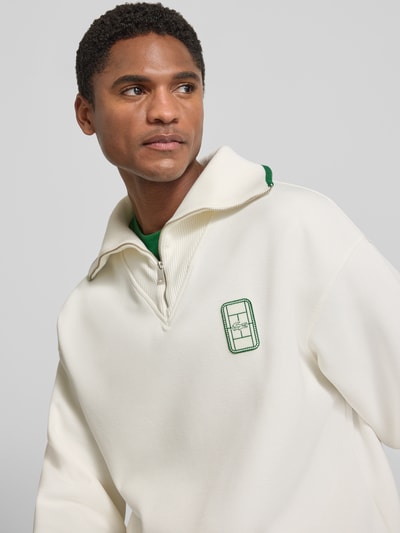 Męski model nosi Loose Fit Troyer aus Baumwoll-Mix Model 'Tennisc' von Lacoste, kremowy kolor, tekstura gładka, haft, zbliżenie górnej części ciała, Herren Troyer von Lacoste.