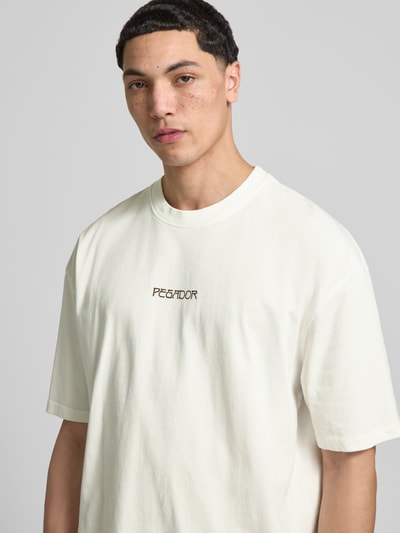 Männermodel trägt Oversized T-Shirt aus Baumwolle Modell 'Stavoren' von Pegador in Weiß, Label-Detail, Halbarm, Nahaufnahme Oberkörper. Herren T-Shirt, Reine Baumwolle, Oversized-Fit, Rundhalsausschnitt, Rückenlänge bei Größe M: 70 cm.