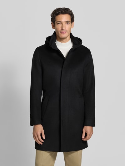 Männermodel trägt Regular Fit Mantel aus reiner Viskose Modell 'Aleric' von Tiger of Sweden in Schwarz, Ganzkörperansicht von vorne. Herrenmantel mit Stehkragen und Kapuze, glatte Textur.
