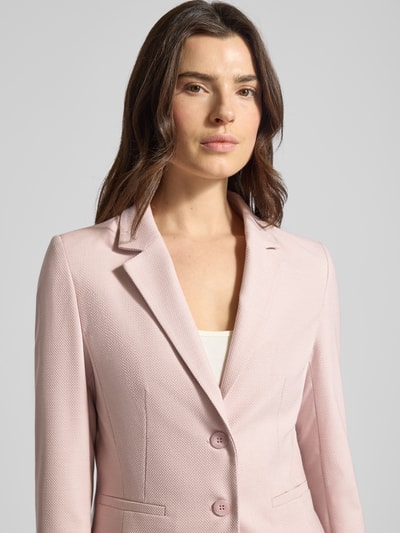 Vrouwenmodel draagt Slim Fit Blazer met reverskraag van More & More in lichtroze materiaalmix met viscose, knoopsluiting, paspelzakken, borstwijdte 46 cm, mouwlengte 64 cm, ruglengte 57 cm, nahaufnahme bovenlichaam.