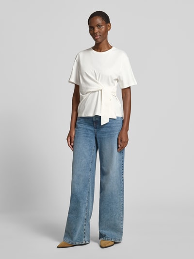 Frauenmodel trägt T-Shirt mit Knoten-Detail und Rundhalsausschnitt von Christian Berg Woman aus Reine Baumwolle, Regular-Fit, Ganzkörperansicht von vorne. Rückenlänge bei Größe S: 55 cm.