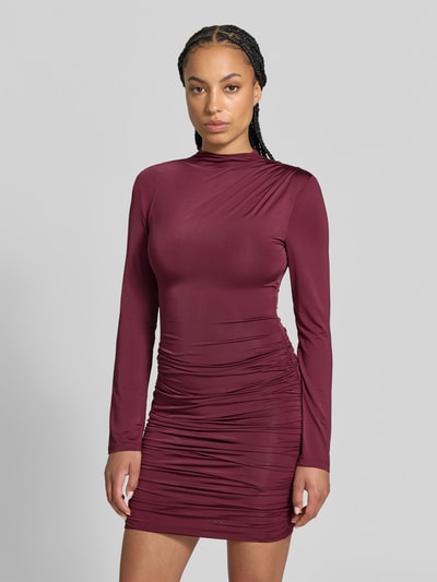 Frauenmodel trägt Slim Fit Minikleid aus Viskose-Mix von ROTATE in Bordeauxrot, Struktur mit Raffungen, Stehkragen, Langarm, Ganzkörperansicht von vorne.