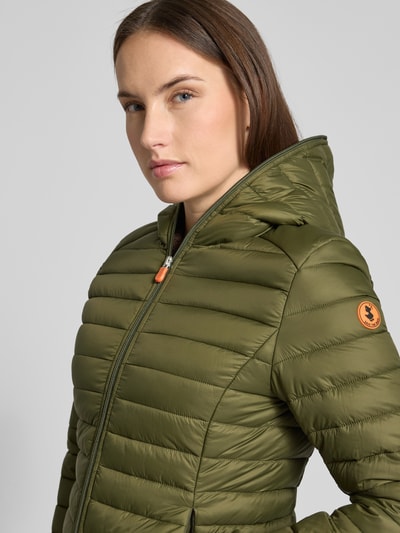 Frauenmodel trägt olivegrüne Steppjacke mit Kapuze Modell 'DAISY' von SAVE THE DUCK, glatte Oberfläche, Reißverschluss, Nahaufnahme Oberkörper.