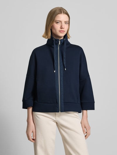 Modelka nosi Regular Fit Sweatjacke mit Viskose-Anteil od Tom Tailor, ciemnogranatowa, krój regular fit, suwak, stojący kołnierz, 3/4 rękawy, kieszenie boczne, scuba, widok na całą sylwetkę z przodu.