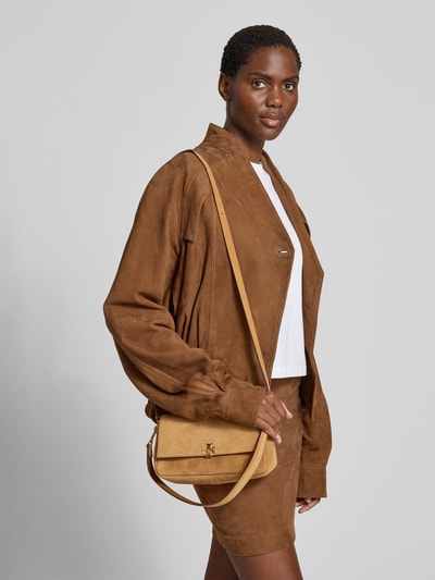 Frauenmodel trägt Shoulder Bag in Suede-Optik von Tory Burch in Beige mit Logo-Detail, abnehmbare Schulterriemen, Ganzkörperansicht von vorne. Breite: 24 cm, Länge: 12 cm, Tiefe: 8 cm, Hauptfach mit Überschlag, Innenfach mit Reißverschluss.
