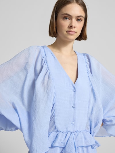 Frauenmodel trägt Minikleid mit Rüschenbesatz von Gina Tricot in Hellblau, V-Ausschnitt, Knopfleiste, Langärmelig, Nahaufnahme Oberkörper. Rückenlänge bei Größe S: 80 cm, Brustweite bei Größe S: 40 cm, Ärmellänge bei Größe S: 62 cm, taillierte Passform, feine Textur.