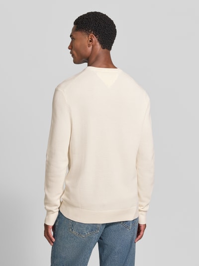 Męski model nosi Regular Fit Pullover aus reiner Baumwolle von Tommy Hilfiger w kolorze kremowym, widok całej sylwetki z tyłu.