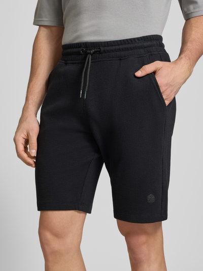 Męski model nosi Straight Fit Shorts mit Logo-Stitching Modell 'Fillip' od Blend, czarny, bawełna, fakturowany, kieszenie, elastyczny pas, szerokość w rozmiarze M: 39 cm, długość nogawki wewnętrznej: 26 cm, ujęcie z przodu, zbliżenie na dolną część ciała.