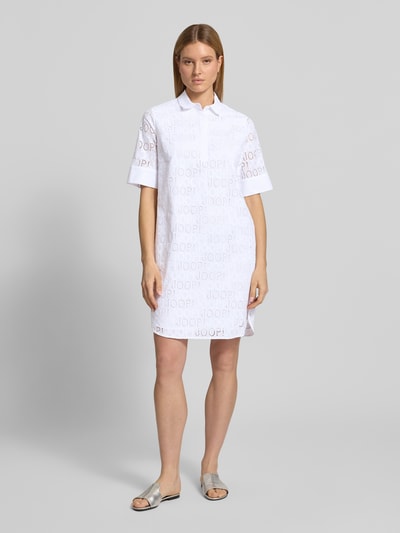 Modelka nosi sukienkę koszulową z czystej bawełny JOOP! Knielanges Hemdblusenkleid mit Logo-Muster Modell 'Deria', prosty krój, długość do kolan, wzór z logo, kołnierzyk koszulowy, rękaw o dł. 1/2, kolor biały. Ganzkörperansicht von vorne.