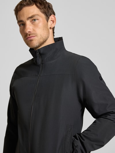 Männermodel trägt Regular Fit Jacke mit Stehkragen Modell 'Alvin' von Didriksons in Schwarz, glatte Textur, Nahaufnahme Oberkörper.