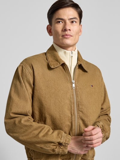Männermodel draagt Regular Fit Bomberjacke aus reiner Baumwolle van Tommy Hilfiger in uni bruin denim, elastische boorden, logo-detail, Nahaufnahme Oberkörper.