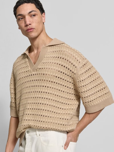 Männermodel trägt Relaxed Fit Poloshirt mit Viskose-Anteil von MAISON KITSUNÉ, beige, Strick-Optik mit Lochmuster, Nahaufnahme Oberkörper. Baumwoll-Viskose-Mix, Umlegekragen mit V-Ausschnitt, Halbarm, Rückenlänge bei Größe M 74 cm.