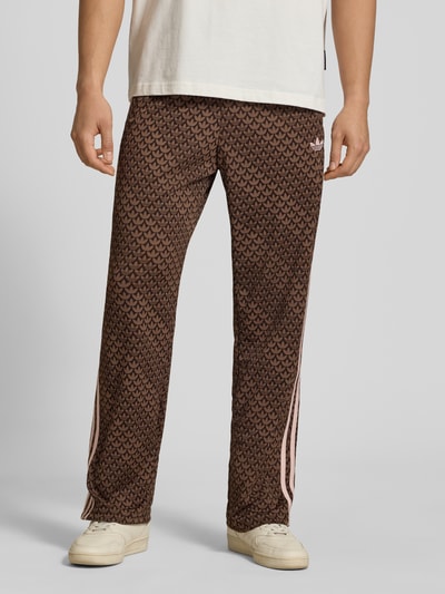 Męski model nosi Loose Fit Sweatpants mit Logo-Muster Modell 'FIREBIRD' von adidas Originals, efekt: wzór z logo na całej powierzchni, krój loose fit, wyhaftowane logo, elastyczny ściągacz z tunelem, boczne kieszenie zapinane na zamek błyskawiczny, wykończenie: dzianina dresowa, Ganzkörperansicht von vorne.