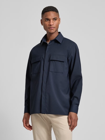 Männermodel trägt Relaxed Fit Hemdjacke mit Schurwoll-Anteil Model 'Arion' von DIGEL in Dunkelblau, Brusttaschen, Umlegekragen, Sportmanschetten, elastischer Material-Mix, Ganzkörperansicht von vorne.