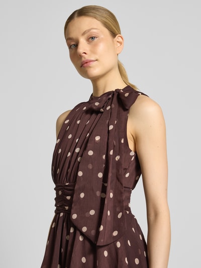 Modelka kobieca nosi 'Abendkleid im Stufen-Look' od Neo Noir, ciemnobrązowy materiał z jasnymi grochami, krój taliowany, okrągły dekolt, maksi długość, kluczowy dekolt z tyłu, długość tyłu w rozmiarze 36: 141 cm, szerokość w rozmiarze 36: 42 cm, ujęcie z przodu w zbliżeniu na górną część ciała.
