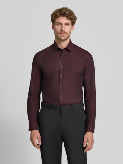 Männermodel trägt Body Fit Businesshemd aus Baumwoll-Mix von OLYMP in Dunkelrot mit schwarzen Stoffhosen, Ganzkörperansicht von vorne. Herren Businesshemd von OLYMP Level 5.