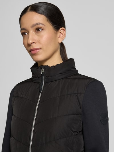 Frauenmodell trägt Slim Fit Steppjacke mit gefüttertem Stehkragen von Christian Berg Woman Selection, Schwarz, Nahaufnahme Oberkörper. Stepp-Optik, Kapuze mit Stehkragen, Reißverschluss, Eingrifftaschen, figurbetonter Schnitt, glatte Struktur.