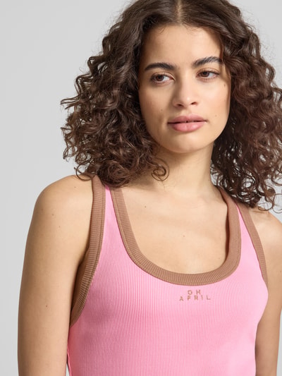Frauenmodel trägt Slim Fit Top mit Logo-Stitching Modell 'Fiora' von OH APRIL in Rosa mit braunen Kanten, Strukturmuster, Nahaufnahme Oberkörper.