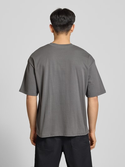 Männermodel trägt Oversized T-Shirt mit Logo und Rundhalsausschnitt van REVIEW in grijs, puur katoen, oversized fit, ruglengte maat M 68 cm, Ganzkörperansicht Rückansicht
