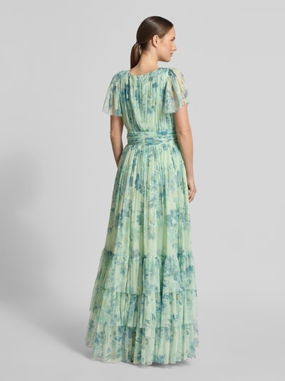 Frauenmodel trägt Regular Fit Abendkleid mit Rüschenbesatz von LACE & BEADS, floraler Allover-Print auf grün-blauem Mesh, Ganzkörperansicht Rückansicht.