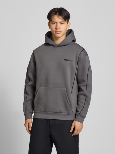 Männermodel trägt Hoodie mit Logo und Känguru-Tasche von REVIEW in Grau, Baumwoll-Mix, Regular-Fit, Ganzkörperansicht von vorne. Rückenlänge bei Größe M: 71 cm, Ärmellänge bei Größe M: 67 cm.