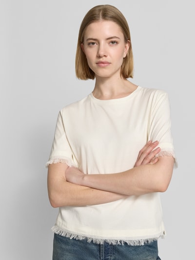 Kobiece modelka nosi T-Shirt aus Leinen mit Fransen od Marc Cain, czysta len, prosty krój, okrągły dekolt, frędzle, nadruk logo, długość tyłu w rozmiarze 36: 55 cm, jasny kolor, tekstura lnu, widok całej sylwetki z przodu.