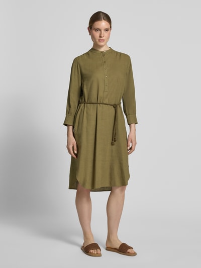 Frauenmodel trägt Midikleid aus Leinen-Mix mit Bindegürtel von Fynch-Hatton, olivgrün, Knopfleiste, Mao-Kragen, Ganzkörperansicht von vorne. Taillierter Schnitt, Leinen-Viskose-Anteil, abgerundeter Saum, Rückenlänge 112 cm, Brustweite 52 cm, Ärmellänge 52 cm.