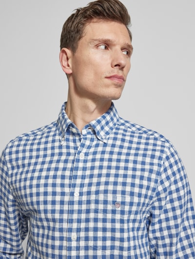Mężczyznę model nosi Regular Fit Leinenhemd mit Baumwoll-Anteil Modell 'GINGHAM' von Gant, niebiesko-biała krata, krój regular fit, button-down kołnierzyk, kieszonka z logo, długi rękaw, mieszanka lnu i bawełny, perspektywa zbliżenie na górną część ciała.