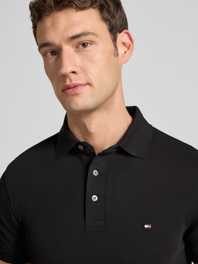 Männermodel trägt Slim Fit Poloshirt mit Stretch-Anteil van Tommy Hilfiger, katoen-elastaan mix, korte knoopsluiting, Nahaufnahme Oberkörper.
