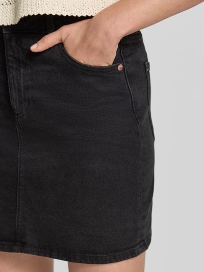 Frauenmodel trägt Regular Fit Jeansrock aus Baumwoll-Mix Modell 'TESSA' von Vero Moda in schwarzem Denim mit 5-Pocket-Design, Nahaufnahme Oberkörper.