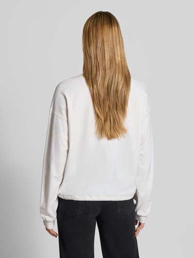 Frauenmodel trägt Relaxed Fit Langarmshirt aus reine Baumwolle von DRYKORN in Weiß, weiche Textur, gerippte Bündchen, Tunnelzug, Ganzkörperansicht Rückansicht.