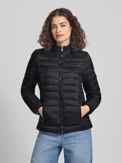 Frauenmodel trägt schwarze Steppjacke mit Logo-Stitching Modell 'FUJI' von Superdry, Gerader-Schnitt, Stehkragen, Reißverschluss, Seitliche Reißverschlusstaschen, Nahaufnahme Oberkörper. Rückenlänge 62 cm, Schulterbreite 40 cm, Brustweite 50 cm, Ärmellänge 69 cm.