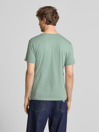 Männermodel trägt T-Shirt mit Label-Detail von Alpha Industries in Grün aus Reine Baumwolle, Gerader-Schnitt, Ganzkörperansicht Rückansicht.
