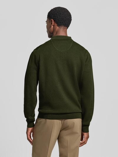 Männermodel trägt Strickpullover mit Polokragen und Knopfleiste von Fynch-Hatton in Dunkelgrün zu beigefarbener Hose, reine Baumwolle, Rückenlänge und Ärmellänge bei Größe M, Regular Fit, Label-Stitching, Ganzkörperansicht Rückansicht.