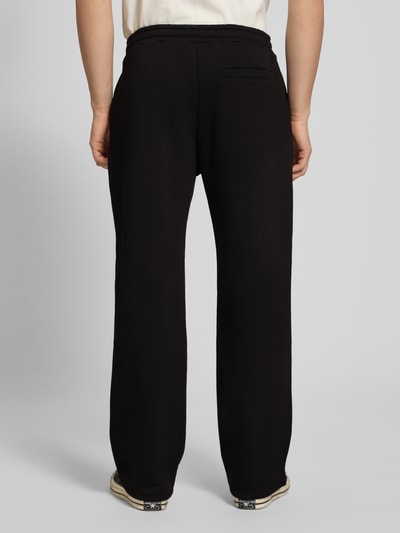 Männermodel trägt Sweatpants mit Logo-Print und Gesäßtasche von REVIEW, schwarze Farbe, Baumwoll-Mix, Gerader-Schnitt, Ganzkörperansicht Rückansicht.