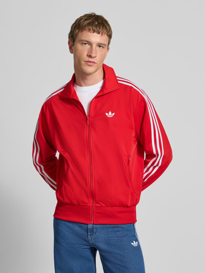 Männermodel trägt Sweatjacke mit Logo-Stitching Modell 'FIREBIRD' von adidas Originals in Rot, Gerader-Schnitt, Stehkragen, Ganzkörperansicht von vorne.